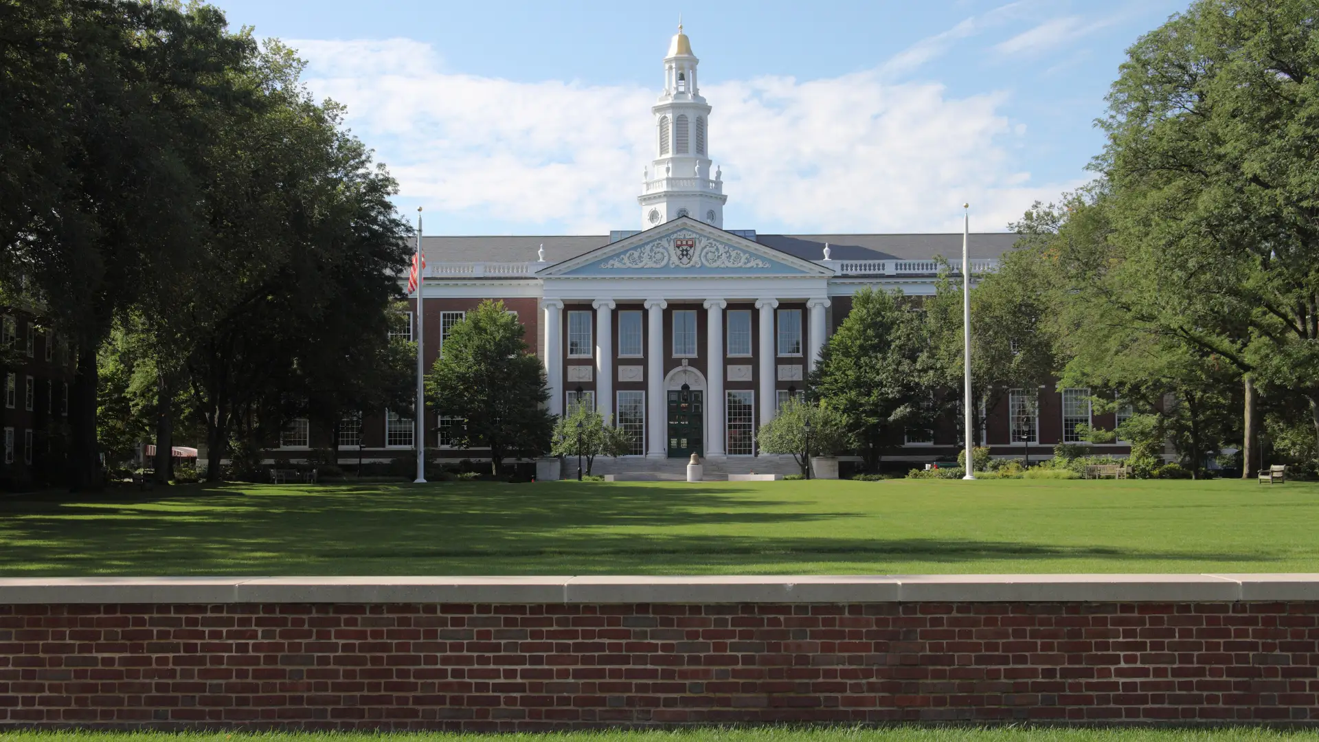 Harvard-style university campus with iconic white-columned building, golden steeple, pristine green lawn, and American flag